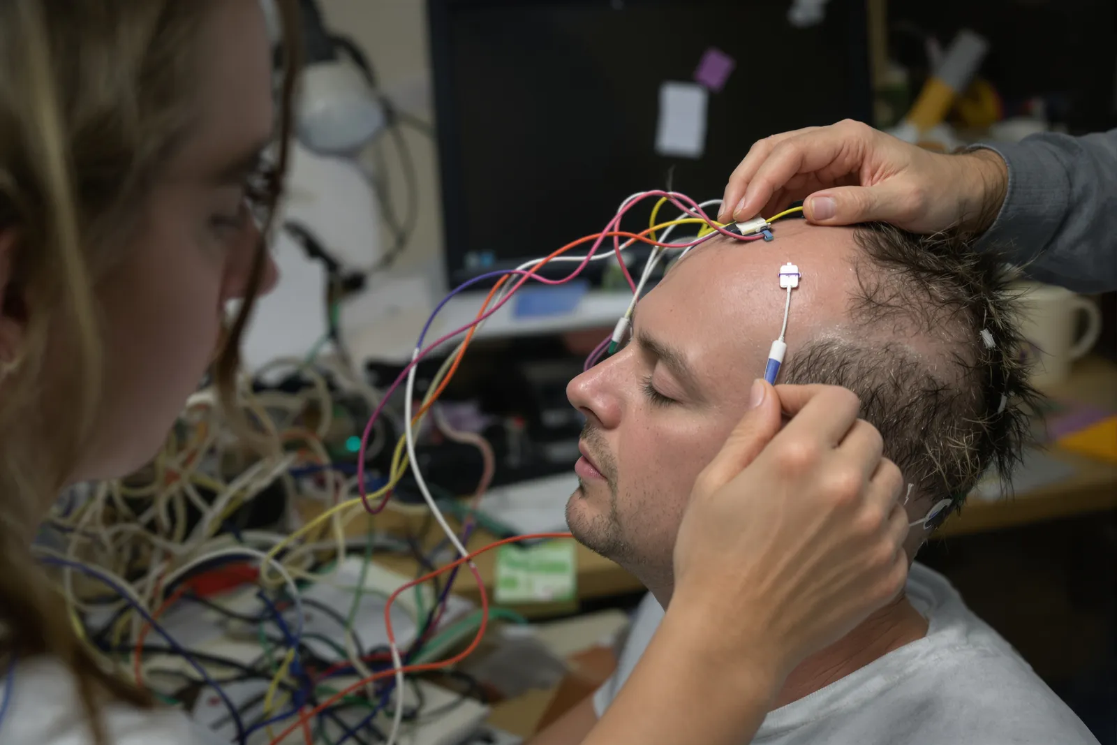 Forscherin justiert eine Elektrode an der EEG-Haube einer Studienteilnehmerin, Hirnmessung in einer Hypnose-Studie