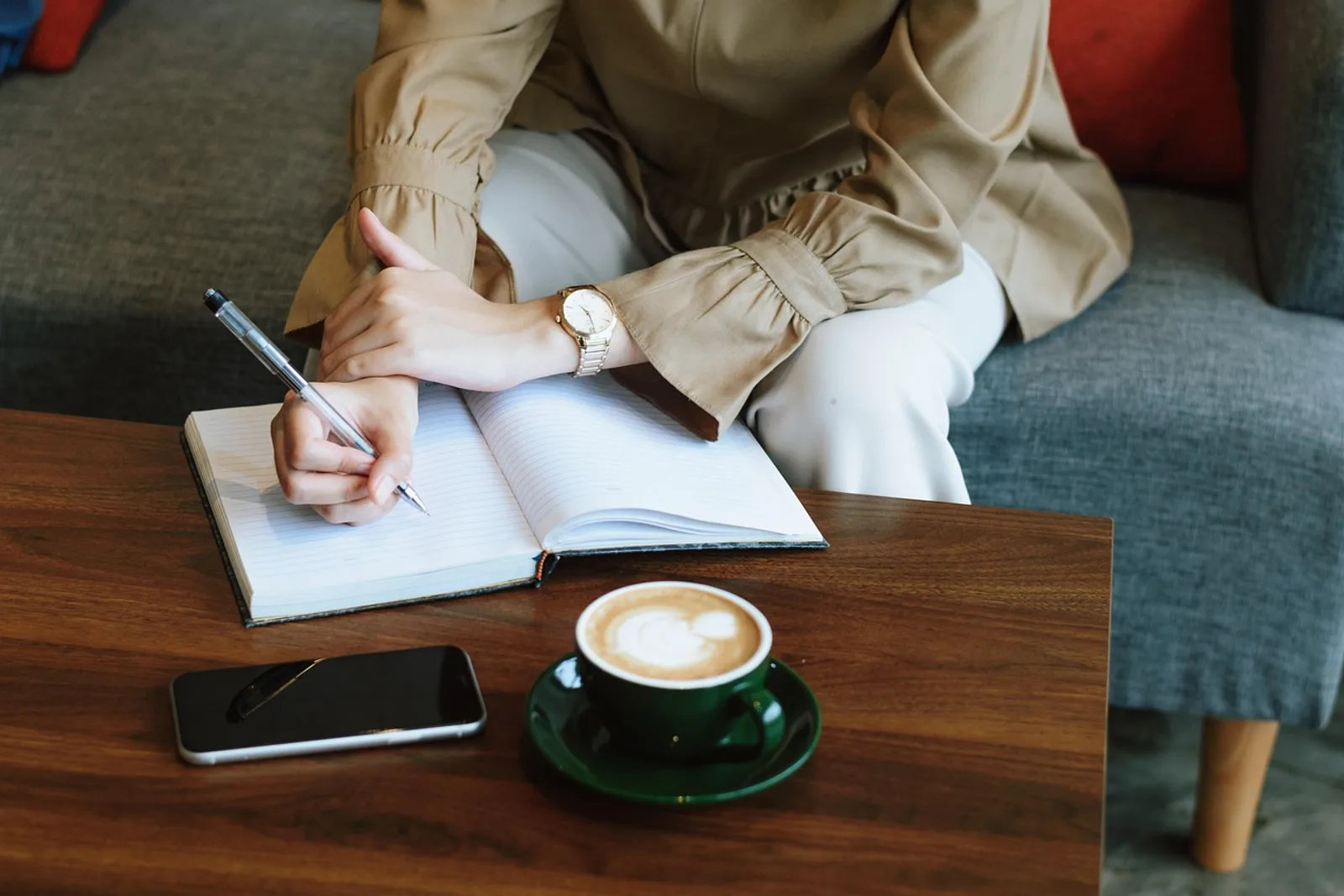 Frau schreibt am Couchtisch in ein Notizbuch, daneben Kaffee – Aufgaben priorisieren lernen beginnt mit einer Liste