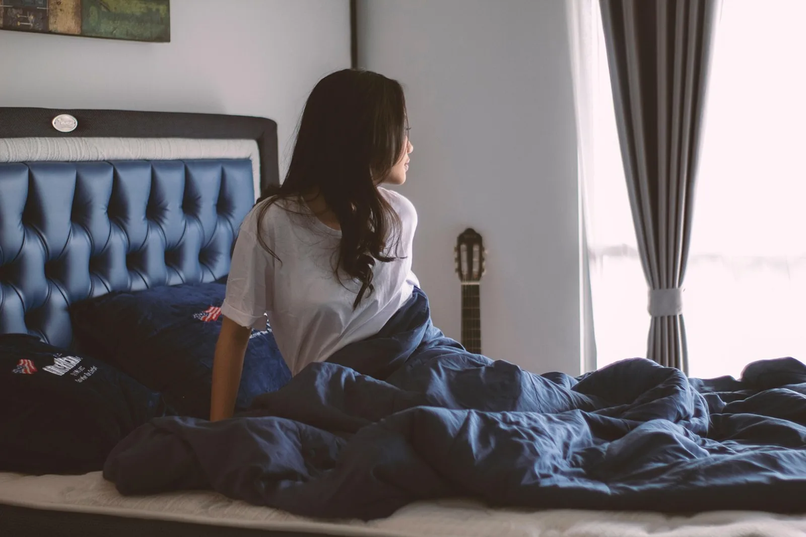 Aufhören sich zu vergleichen: Frau sitzt morgens im Bett und schaut still zum Fenster