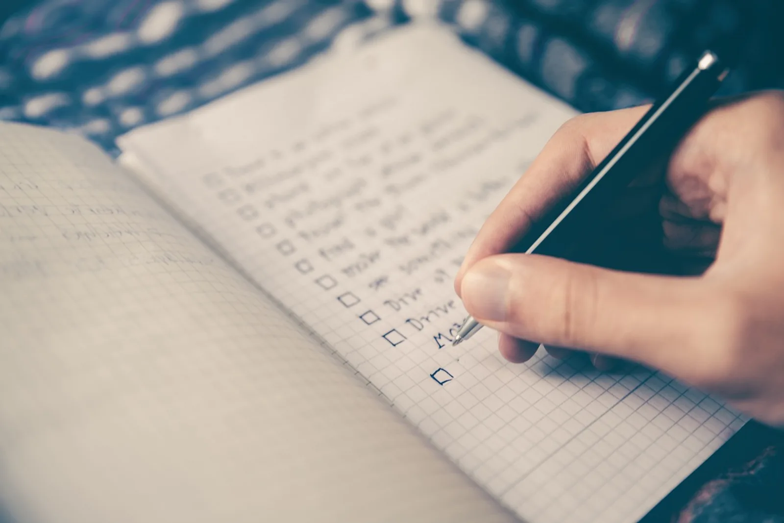 Hand schreibt einen weiteren Punkt auf eine lange To-do-Liste mit leeren Kästchen. Dinge zu Ende bringen statt anhäufen